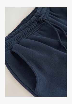 Marineblauwe fleece shorts met een gegatherde tailleband, trekkoorddetail en zijzakken; zachte textuur en een schoon, minimalistisch ontwerp.
