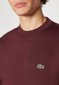 Burgunderfarget bomull crewneck sweatshirt har en teksturert overflate og en brodert grønn krokodillelogo på venstre bryst.
