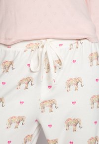 Ljusrosa topp med mönstrade vita pyjamabyxor som har blommiga elefanter och rosa hjärtan, snörning i midjan och mjukt bomullstyg.