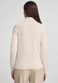 Lichtbeige gebreide trui met een col en geribde boorden bij de mouwen en zoom. De stof voelt zacht aan en heeft een licht gestructureerd oppervlak, ontworpen voor een comfortabele pasvorm.