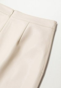Jupe en similicuir couleur crème avec une fermeture éclair au dos et des détails de coutures verticales, présentée à plat sur une surface blanche.