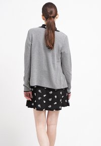 Camicia a maniche lunghe a fantasia grigia con colletto nero, abbinata a una gonna corta nera con stampe floreali e paisley bianche.