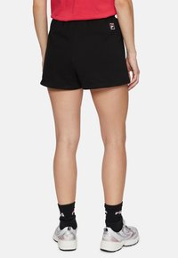 Svarta bomullsshorts med elastisk midja, med en liten logotyp på baksidan, i kombination med vita sneakers och svarta strumpor.