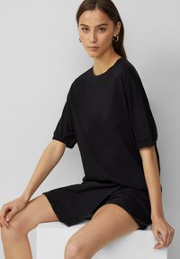 Czarna sukienka krótko rękawowa, wykonana z bawełny, z marszczonymi rękawami, luźnym krojem i długością do kolan z delikatnie postrzępionym brzegiem.