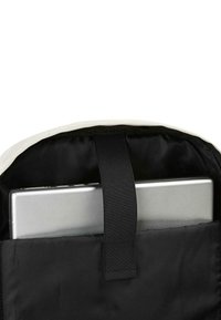 La bolsa para laptop se abre, revelando un laptop plateado asegurado por una correa de tela negra, con un exterior beige y un interior forrado de negro.