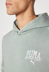 Light green hoodie with a soft texture, featuring a large white "PUMA sports club" logo on the chest and a drawstring hood.
