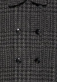 Dwurzędowy płaszcz z teksturowanej szarej tkaniny w wzór houndstooth. Posiada czarne guziki i kołnierz.