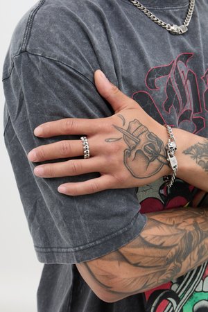 Zilveren schedelring en kettingarmband op een hand met gedetailleerde tatoeages. Grijze, gestructureerde t-shirt met een gedurfde grafisch ontwerp.