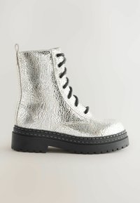 Botte de cheville en cuir argenté craqué avec des lacets noirs, une semelle épaisse et une boucle à l'arrière pour un enfilage facile.