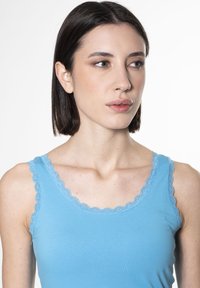 Top estivo blu chiaro con bordi in pizzo a scallop lungo il colletto e le maniche. Tessuto morbido con un design aderente e dettagli minimi.
