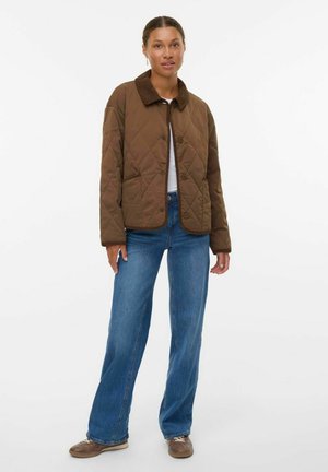 Veste matelassée marron avec un col en velours côtelé, dotée d'une fermeture à boutons et de deux poches avant, associée à un jean bleu à jambes larges et des chaussures marron.