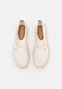 Paire d'espadrilles slip-on blanc cassé avec semelles en corde et petits drapeaux Tommy Hilfiger sur le dessus et semelles intérieures de marque.