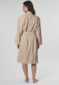Beige terry cloth bathrobe with long sleeves, a belted waist, and a shawl collar, showing a textured surface and mid-calf length.