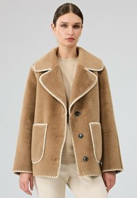 Bruine wollen buitenjas met een schuin gesneden kraag, crèmekleurige accentstiksel, drie knopen en twee voorklassen. Zachte textuur en een comfortabele pasvorm.