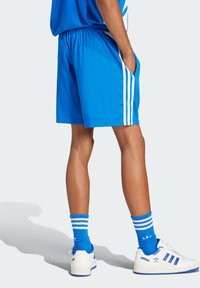 Shorts de sport bleus avec des rayures blanches, dotés d'une taille élastique et de poches latérales. Accompagnés de chaussettes bleues et de baskets blanches.