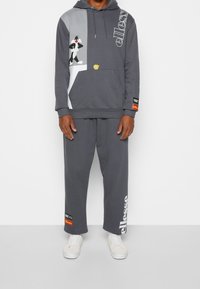 Felpa grigia con cappuccio con grafiche di personaggi dei cartoni, abbinata a pantaloni della tuta coordinati. Presenta logo e dettagli vivaci sul tessuto.
