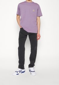 Camiseta de algodón de color púrpura claro con un bolsillo en el pecho, combinada con jeans de mezclilla negros y zapatillas blancas con acentos azules.