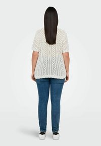 Cremefarvet blonderet top med korte ærmer, der har en løs pasform og bølget kant, kombineret med blå stramme jeans og hvide sneakers.