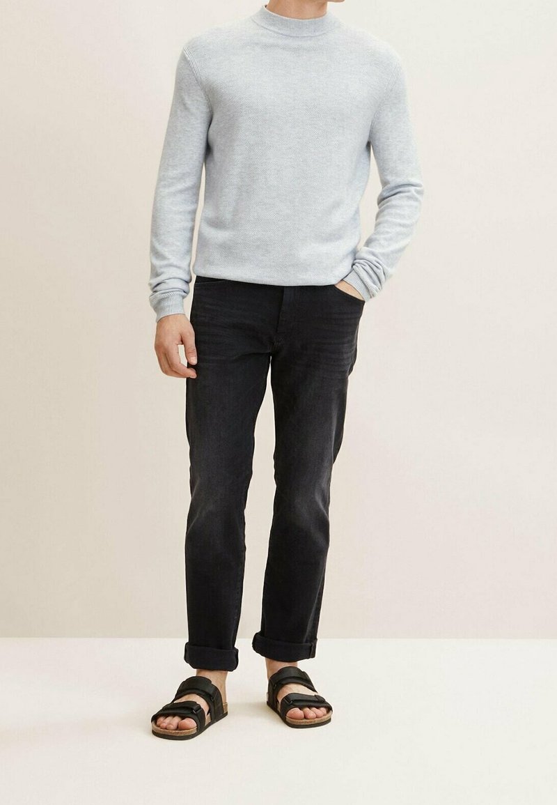 Suéter de punto gris claro, jeans negros con puños enrollados y sandalias negras con tiras. Enfoque en la textura y el diseño casual.