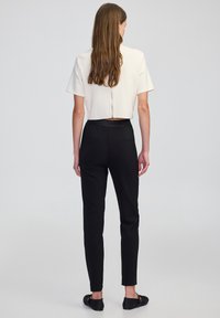 Top blanc cropped avec des manches courtes et une fermeture éclair au dos, associé à un pantalon noir ajusté. Tissu lisse avec une taille cintrée et des poches discrètes.