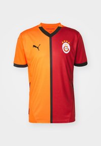 Camiseta de fútbol con mitades naranja y roja, que presenta un collar negro y un ribete en las mangas. Muestra un logotipo y tres estrellas, fabricada con tejido transpirable.