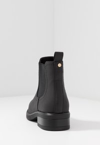 Bottines chelsea noires avec panneaux élastiques sur les côtés, finition mate lisse, bout arrondi et petit talon bloc. Présente un petit accent logo.