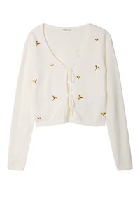White cropped cardigan made of soft material with long sleeves. Features yellow floral embroidery and a tie closure at the neckline.