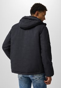 Dark gray hooded jacket with a textured fabric, featuring a straight cut, and zippered front, paired with light blue jeans.