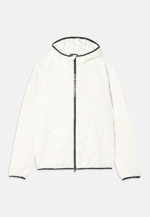 Balts polsterētais mētelis ar kapuci, ar priekšējo rāvējslēdzēju, melniem akcentiem uz kapuces un piedurknēm, kā arī dimanta šūšanas rakstu.