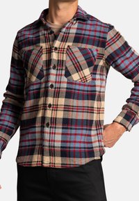 Koszula w kratę w odcieniach beżu, czerwieni i granatu. Posiada guziki, dwie kieszenie na piersi oraz klasyczny kołnierzyk. Wykonana z fakturowanej tkaniny.
