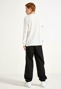 Camicetta bianca a maniche lunghe con un design testurizzato, abbinata a pantaloni neri a vestibilità ampia. L'outfit è completato da scarpe da ginnastica bianche.