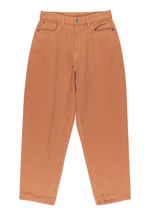 Personne portant un col roulé beige et marron rayé, un pantalon taille haute couleur pêche et des chaussures marron foncé, debout les mains dans le dos.