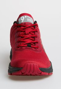 Roter Sportschuh mit strukturierter Oberfläche, schwarzen Akzenten und auffälliger Schnürung. Verfügt über eine gepolsterte Sohle und ein graues Etikett mit der Nummer 19.