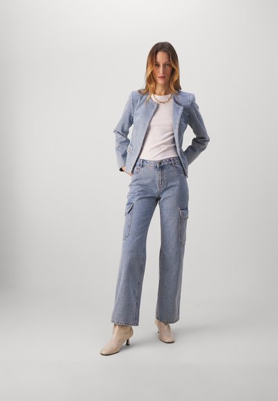 Lyseblå denimjakke med strukturerte skuldre, hvit topp, og lyseblå vide cargo-bukser. Beige hæler fullfører antrekket.
