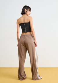 Black cropped strapless top with zip closure, paired with loose-fitting brown satin pants featuring white side stripes.