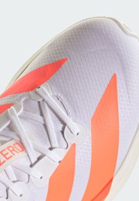 Športová obuv s bielym sieťovaným zvrškom s výraznými oranžovými akcentmi, textúrovaným vzorom a bielymi šnúrkami, navrhnutá pre ľahký výkon.