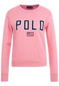 Rosa sweatshirt med ribbade muddar och nederkant. Har "POLO" i marinblå bokstäver och en broderad amerikansk flagga. Mjuk bomullsmaterial.