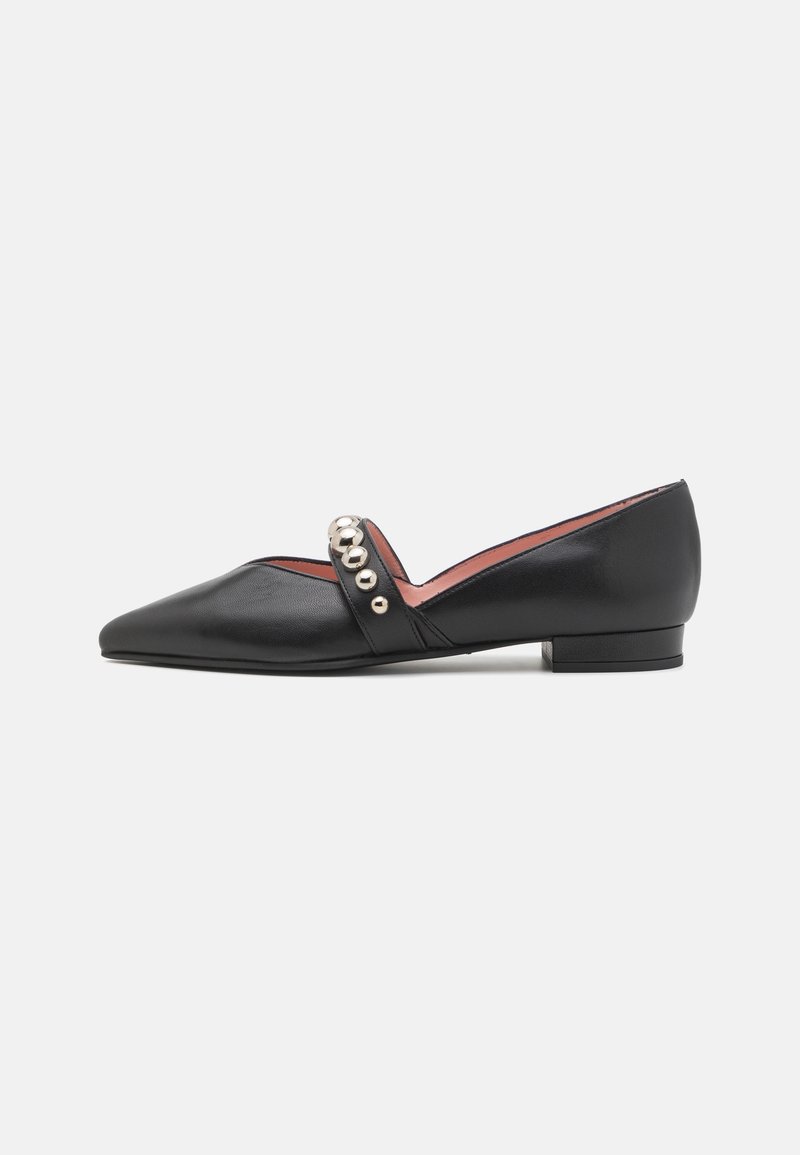 Chaussure plate pointue en cuir noir avec petit talon et bride ornée de cinq clous ronds argentés, sur fond blanc.