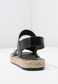Černé kožené sandály s pletenou juteovou podrážkou, s nastavitelnými popruhy a plochým designem. Bez ozdob a vzorů.