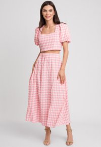 Różowy, w kratkę krótki top z bufiastymi rękawami oraz pasującą długą spódnicą. Materiał wydaje się lekki i ma teksturowane wykończenie, prezentując wzór w gingham.