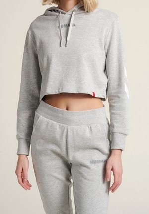 Haut de survêtement cropped gris clair avec cordons et logo, associé à un pantalon de survêtement assorti avec une taille élastique et un détail logo.