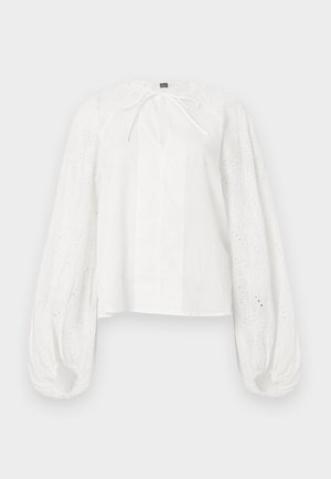 Blouse blanche avec de longues manches bouffantes en dentelle à jours et un petit lien au niveau de l'encolure, présentant une coupe droite et un tissu léger.