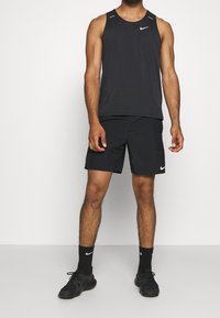 Musta Nike ilmanhiha-urheilutoppi ja shortsit, joissa on sileä ja kevyt kangas. Mustat urheilukengät ja sukat logolla.
