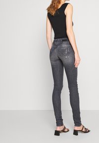Top negro sin mangas, jeans ajustados grises con un lavado desgastado, detalles desgastados y una cintura alta; combinados con sandalias negras de tacón cuadrado y tiras.