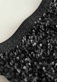 Sort pailletstof med en tekstureret overflade, der har runde pailletter fordelt over materialet. Kantet med en glat sort trim.