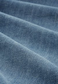 Plis de tissu en denim bleu clair avec une texture tissée, montrant le motif de tissage diagonal et la surface douce du matériau.