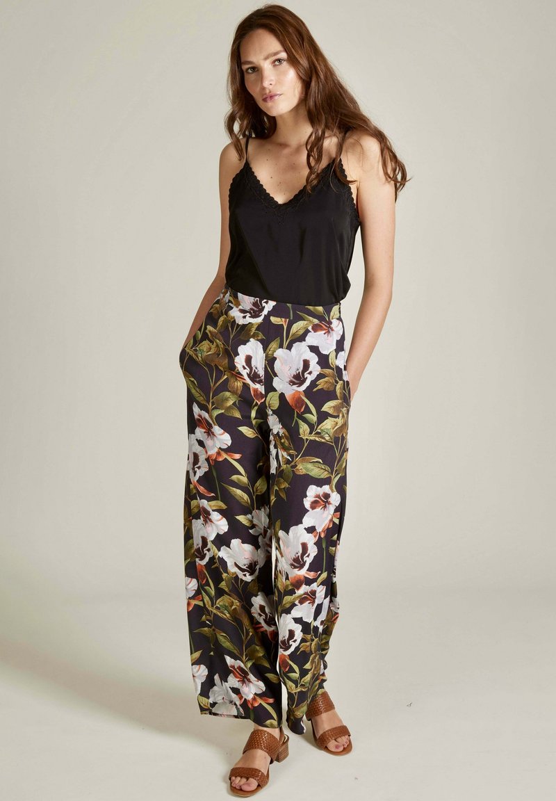 Débardeur noir avecdentelle, associé à un pantalon large à fleurs en tissu sombre avec des fleurs blanches et du feuillage. Sandales à lanières marron.