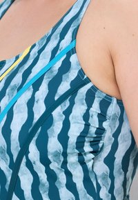 Bañador de una sola pieza con patrones azules en forma de olas, con acentos en azul verdoso y amarillo. Textura suave y diseño de espalda nadadora.