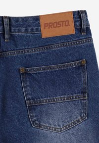 Ciemnoniebieskie dżinsy z denimu z skórzaną metką oznaczoną "PROSTO", z tylną kieszenią z detalami przeszycia i wzmocnioną konstrukcją.