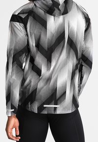 Sort og hvid løbejakke med hætte, der har diagonale striber og zigzag-detaljer på et letvægts, struktureret stof.
